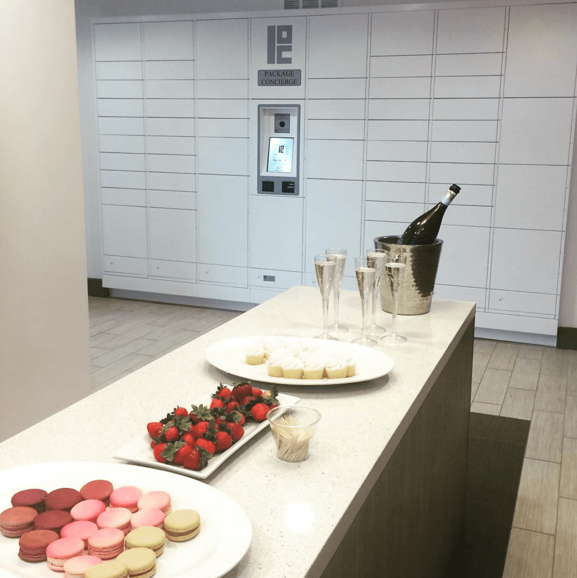 A white Package Concierge® automated locker system in a mailroom with an island covered in champagne glasses, pastries and fruit