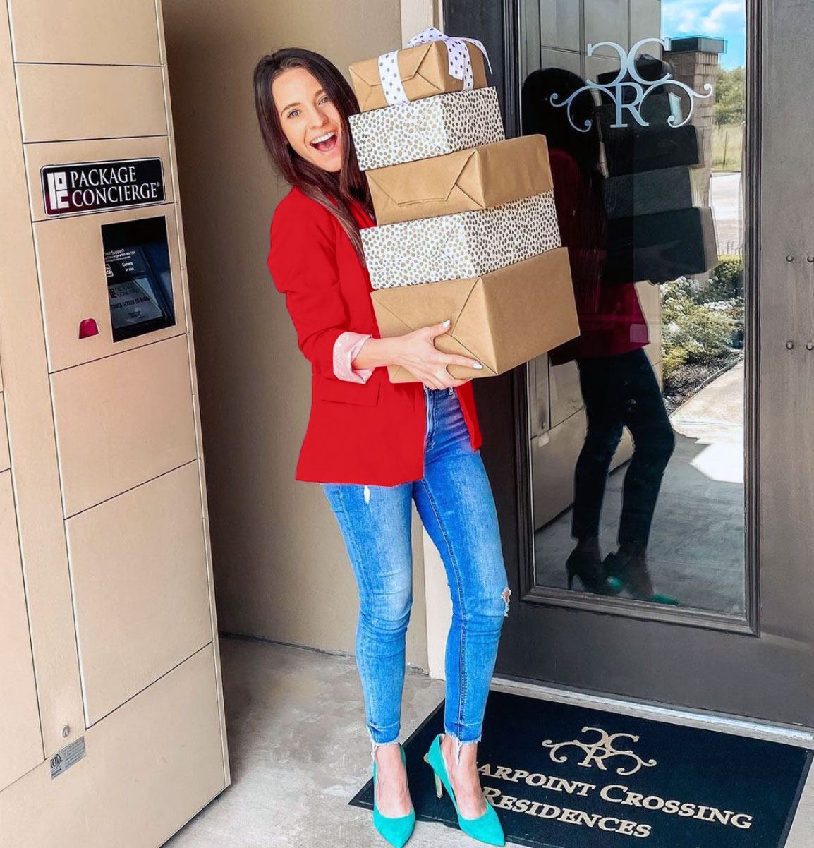 smiling woman in red jacket holding a stack of boxes in front of smart package locker