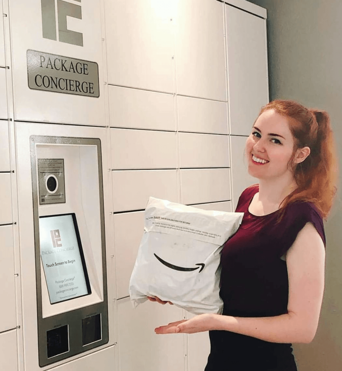 A woman in a maroon shirt is holding an Amazon package in front of a Package Concierge® smart electronic parcel locker