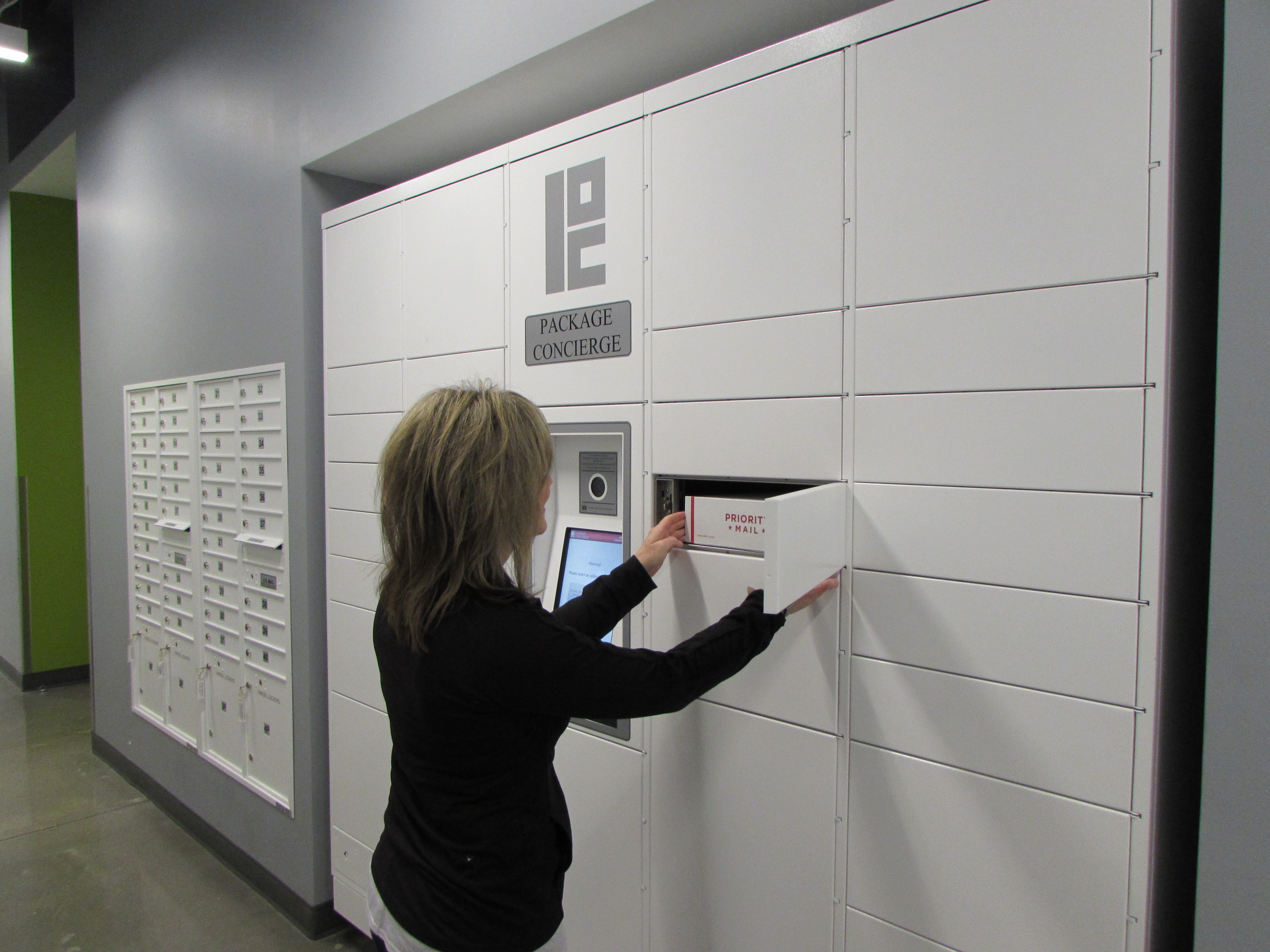 Woman retrieving package from coordinated centralized mailbox and smart package locker center in matching white powdercoat paint